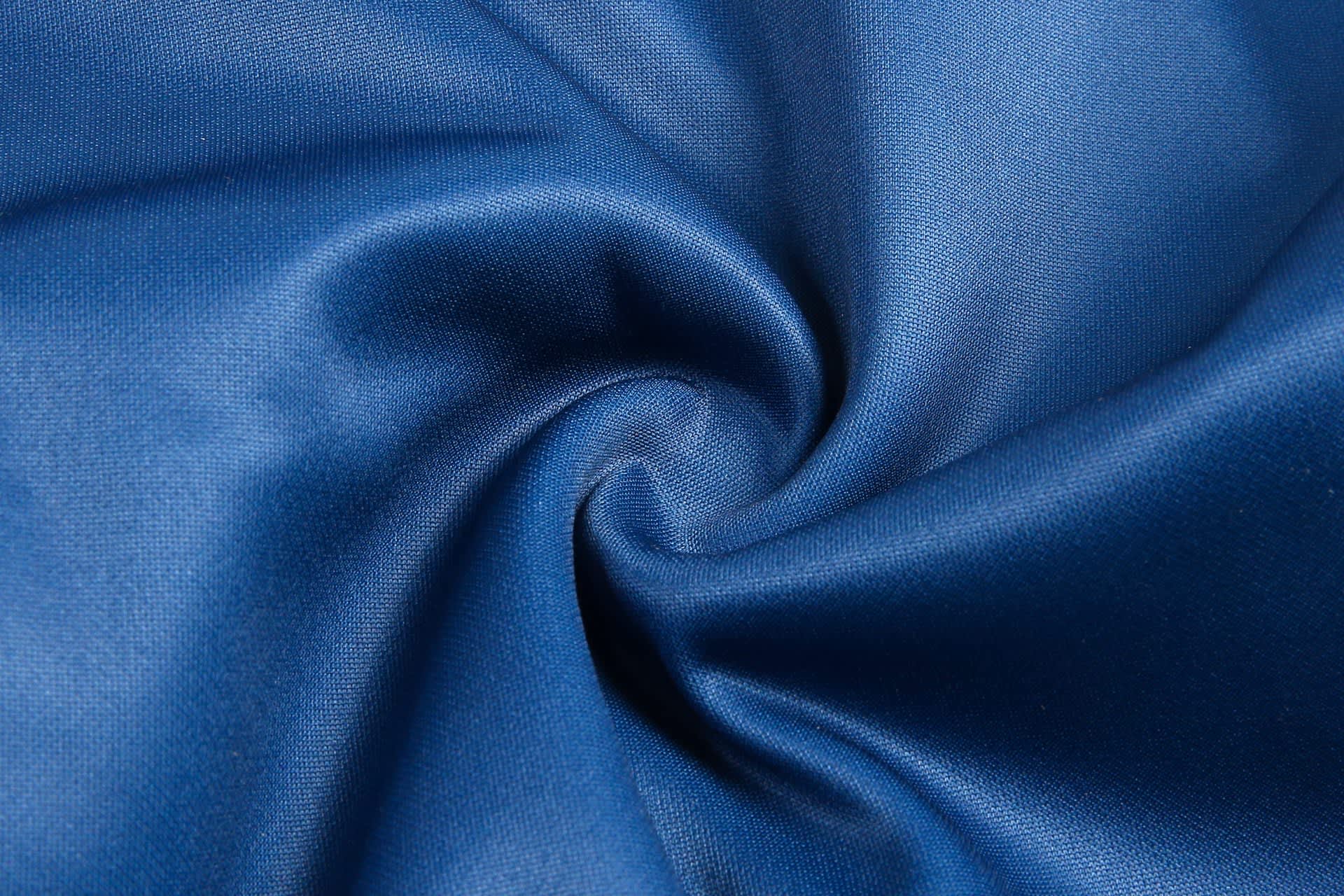 A blue fabric material displayed in a swirl pattern, showcasing a smooth texture. It features a branded logo.