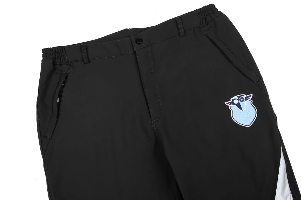 Softshell pants in black with a blue and white logo on the front, featuring an elastic waistband and zippered pockets.
