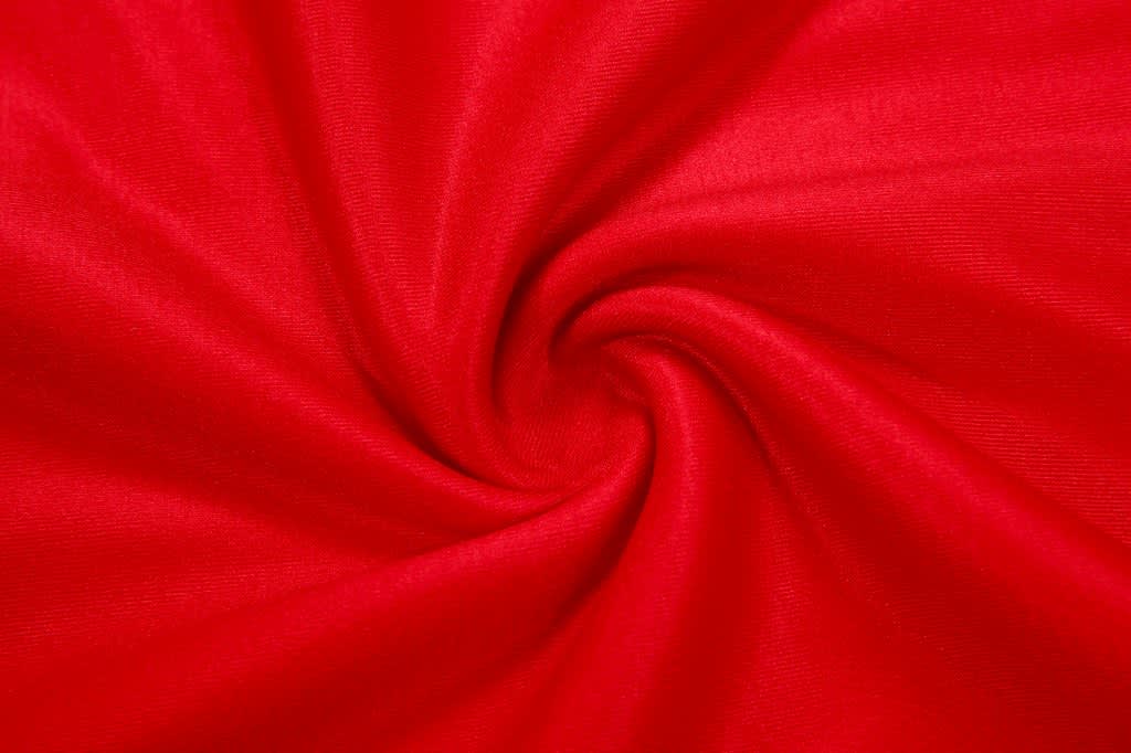A red fabric swirling in a spiral pattern, showcasing its smooth texture and vibrant colour.