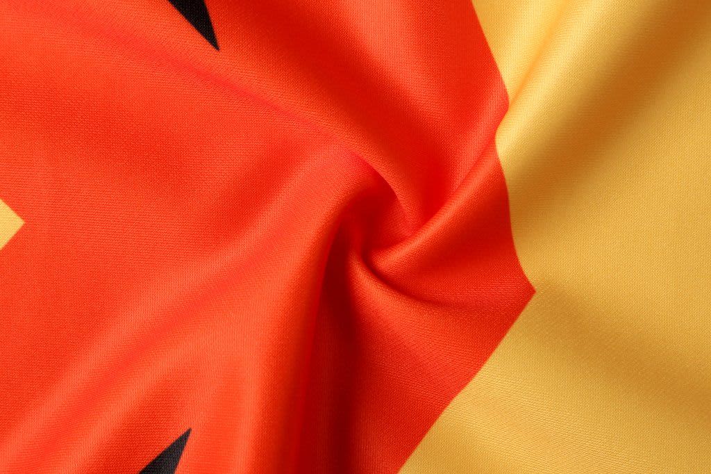 An AFL singlet featuring vibrant red and yellow fabric with black elements and a branding logo.