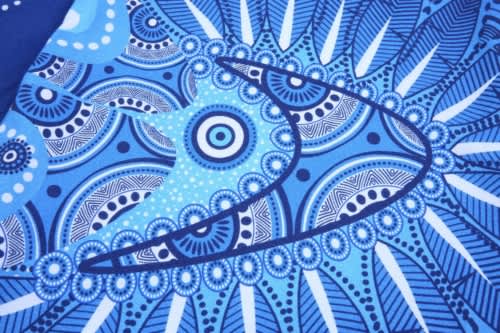 A patterned blue fabric featuring intricate designs and shapes, likely from the Aboriginal Cotton Tee shirt.