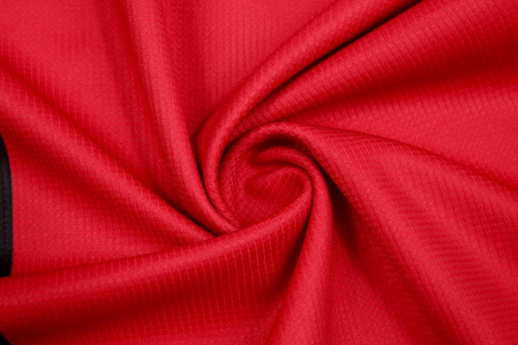 A red fabric with a textured pattern, arranged in a spiral. The material appears lightweight and smooth.