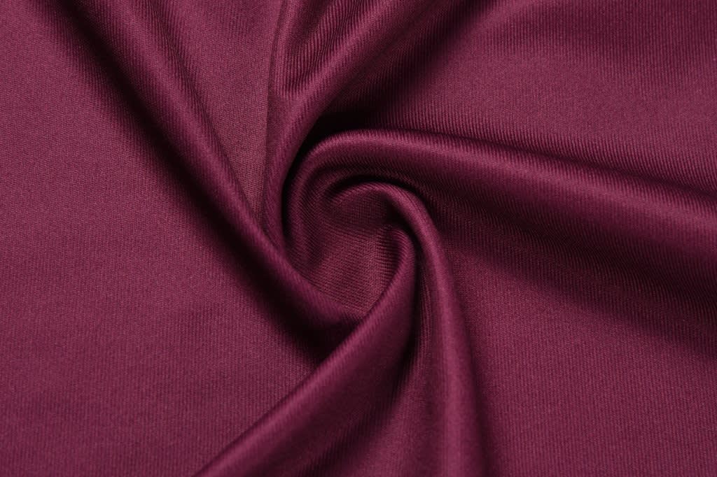A close-up of burgundy fabric, displaying a smooth and stretchy texture with a slight sheen.