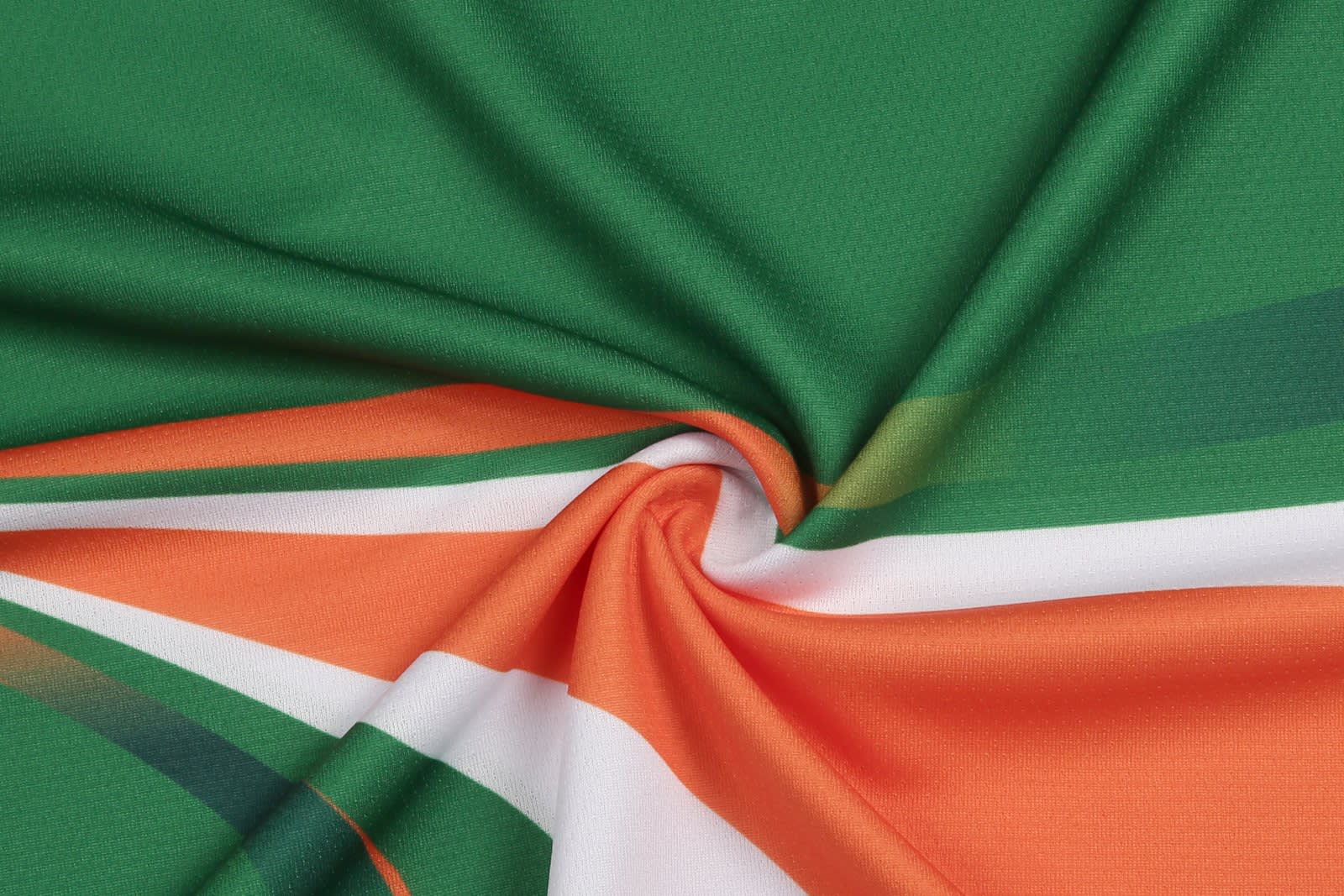 A close-up of a fabric featuring green, orange, and white colours in a smooth texture. The material has a vibrant pattern.