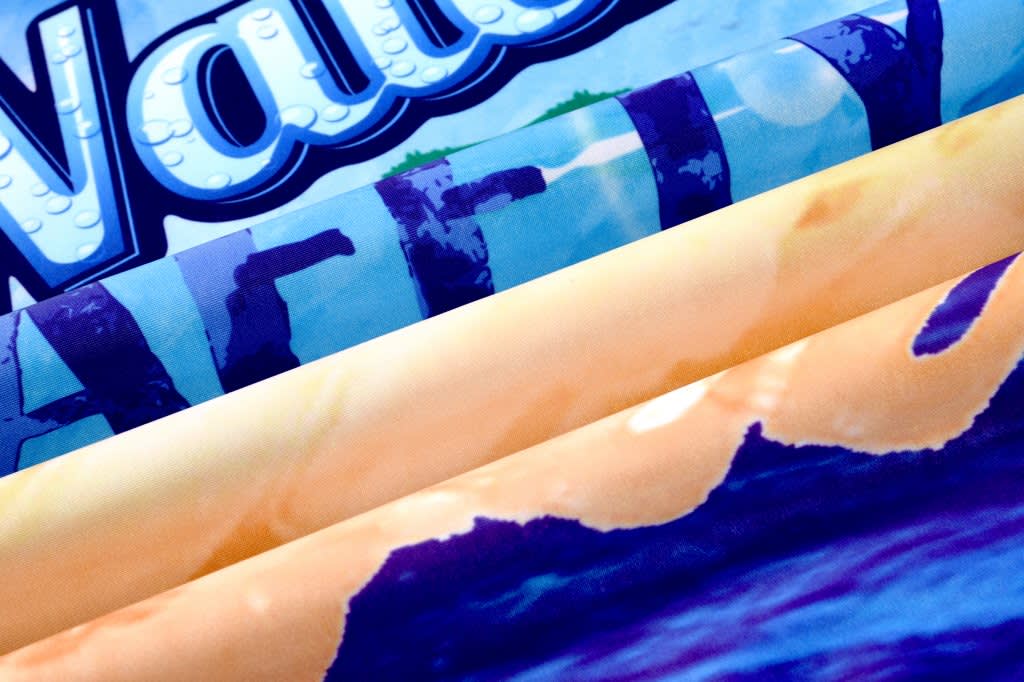 A collection of fabrics in vibrant colours, featuring prints of water and ocean themes, with a logo visible.
