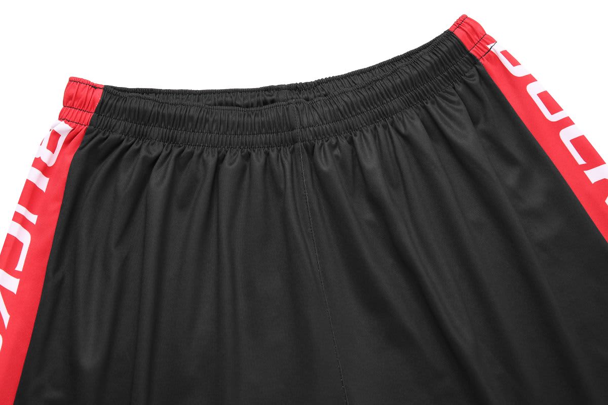 Black shorts with red side panels and an elastic waistband. Features branding on the side.