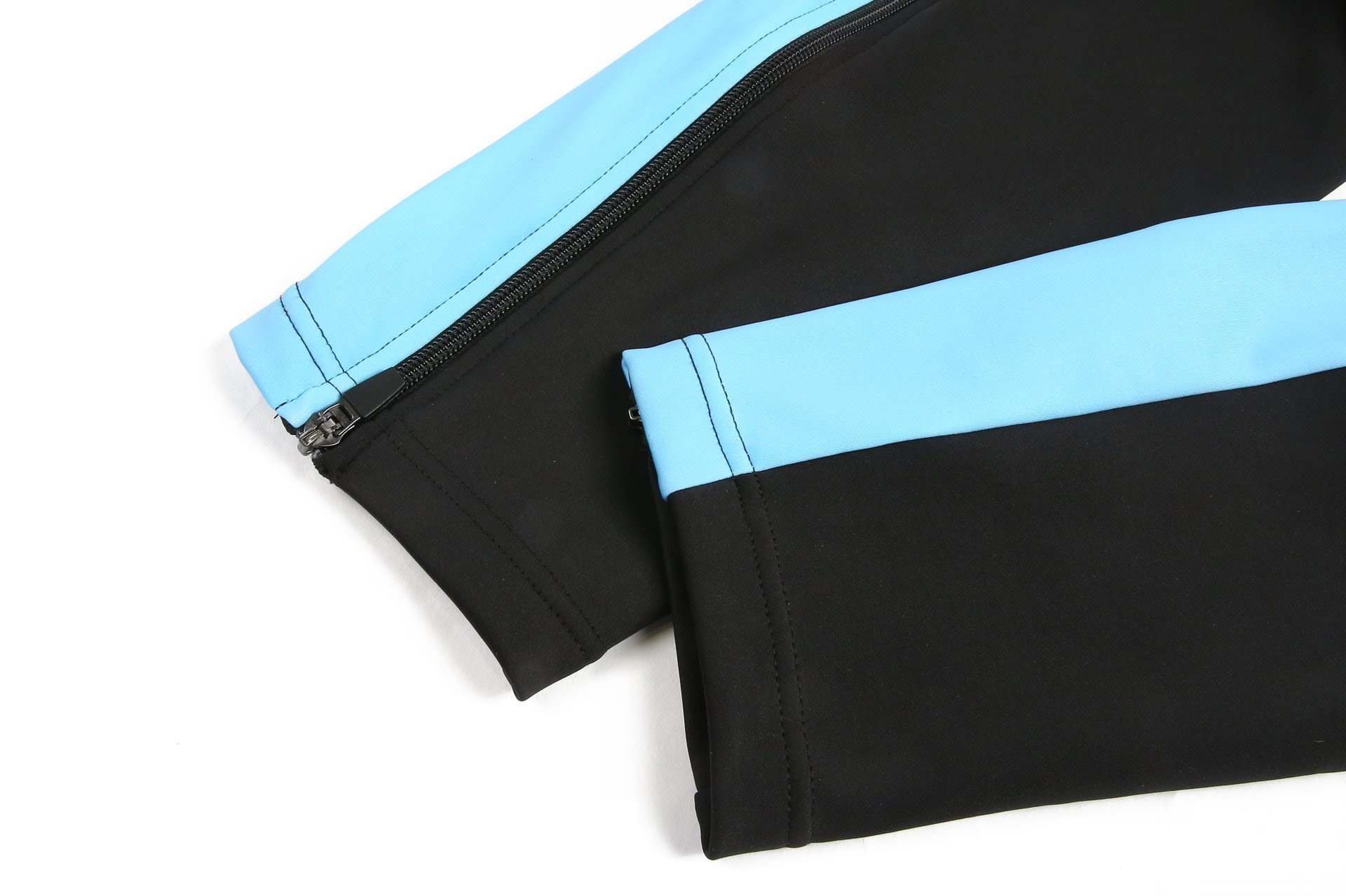 A black and sky blue tracksuit warm-up with zippered cuffs, featuring a logo on the fabric.