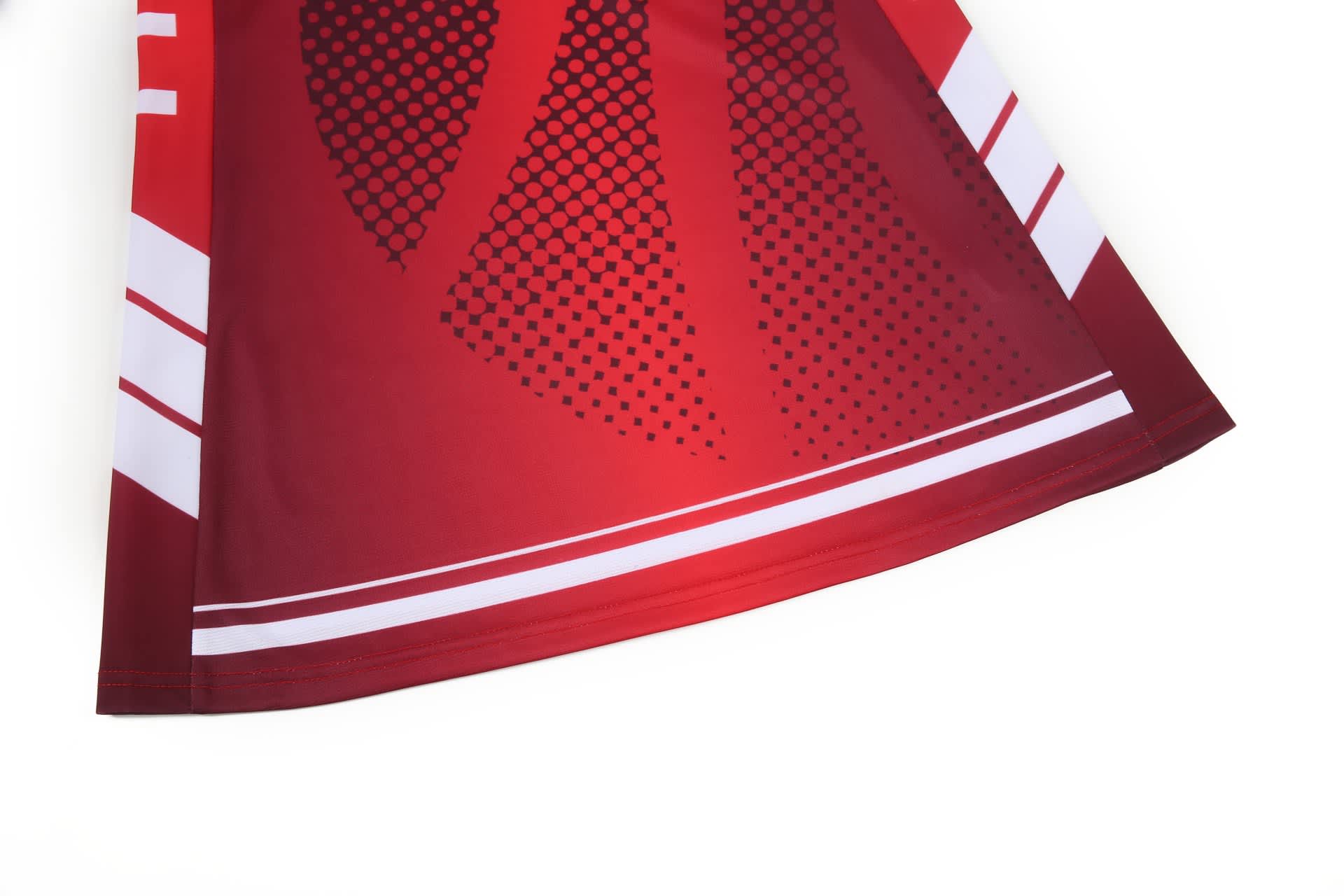 A netball dress in vibrant red with a pattern of dots and stripes, featuring a logo on the fabric.