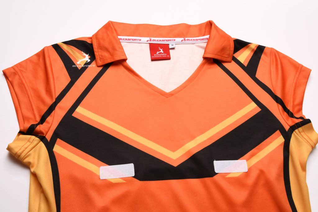 An orange and black polo shirt with angled patterns and a collar, featuring a logo and two white patches.