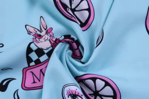 A fabric with a light blue background featuring playful illustrations of a bunny, lemons, and various patterns in pink and black.