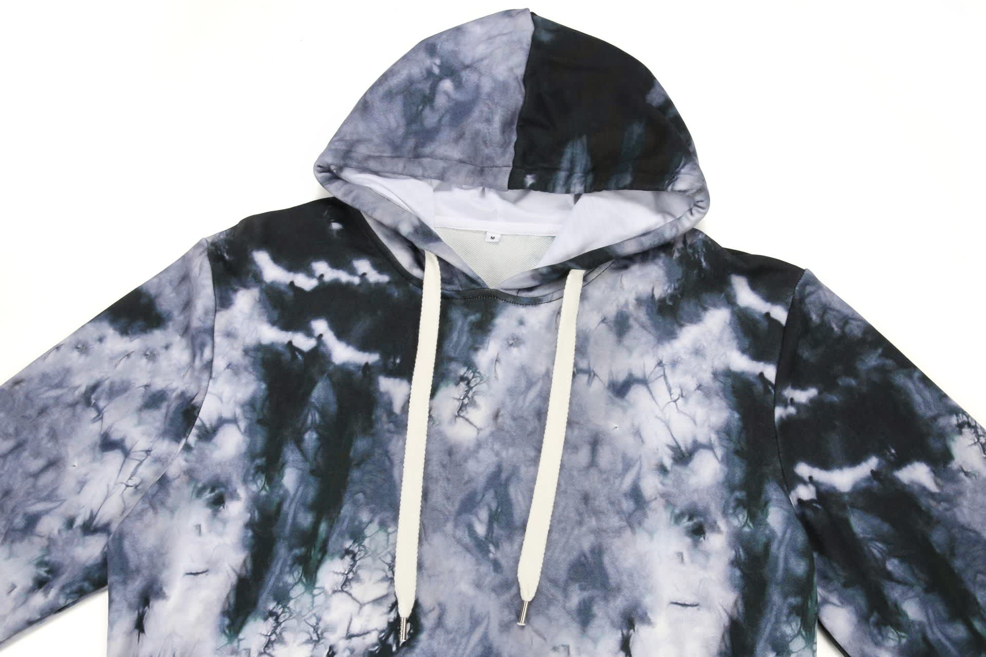 A cotton hoodie featuring a grey and black tie-dye pattern with a drawstring hood and a brand logo.