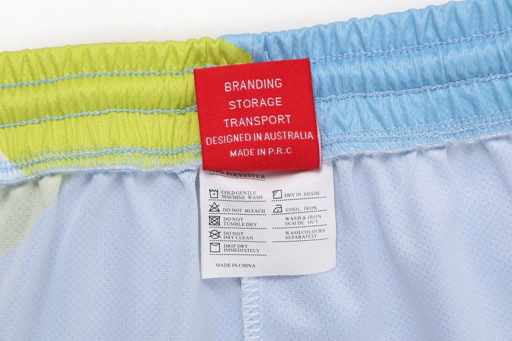 A close-up of the waistband tags on light blue track pants, featuring vibrant green and blue accents.