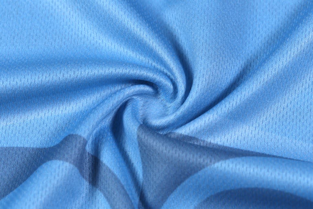 A close-up of a light blue fabric with a subtle texture, featuring a swirl pattern. The material appears breathable.