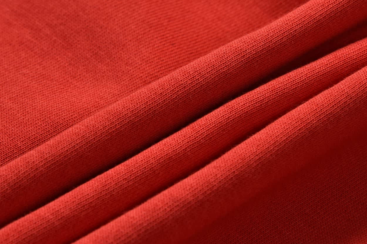 A close-up of red fabric with smooth folds, showcasing a soft texture. The material appears lightweight and inviting.