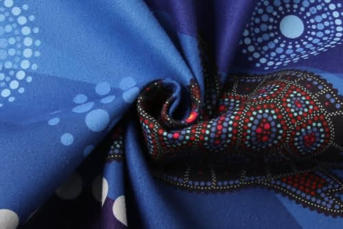 A folded piece of fabric featuring vibrant blue tones with intricate patterns in red and white dots. It has a logo.