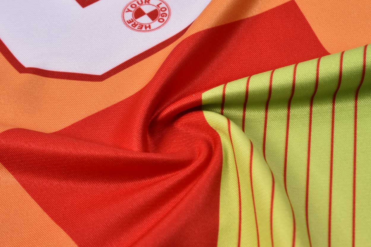 A vibrant football jersey featuring a blend of orange, red, and green colours with a logo.