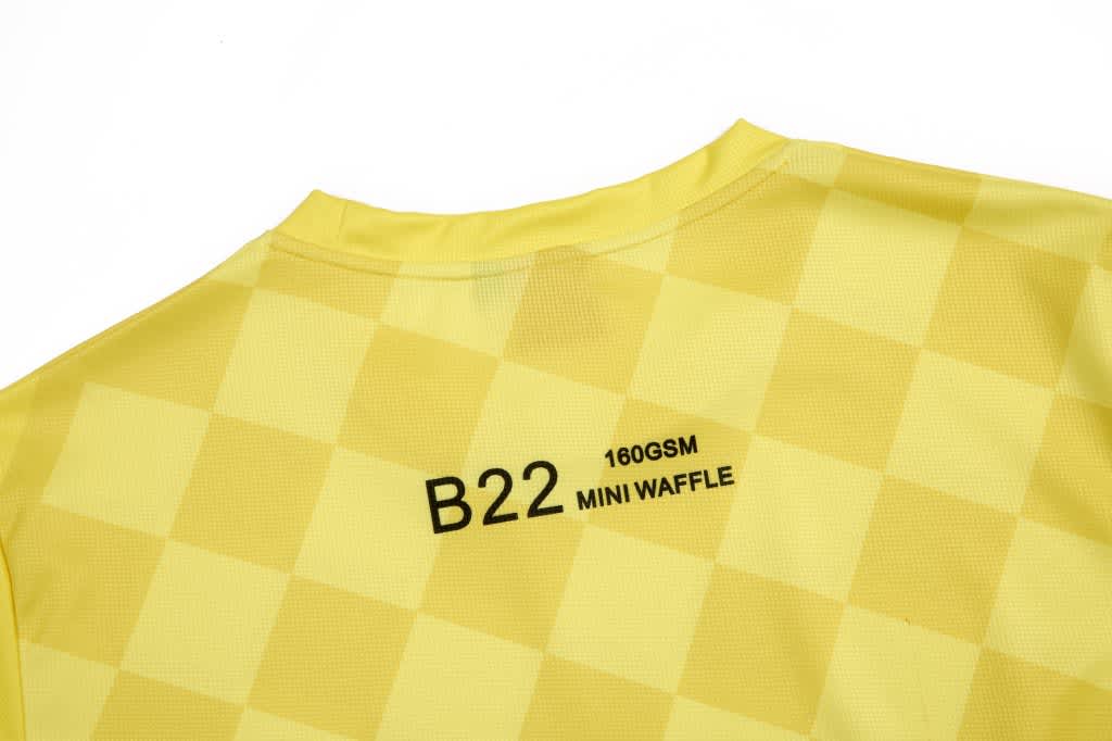A yellow checkered shirt featuring a logo and text on the back. The fabric appears lightweight and textured.