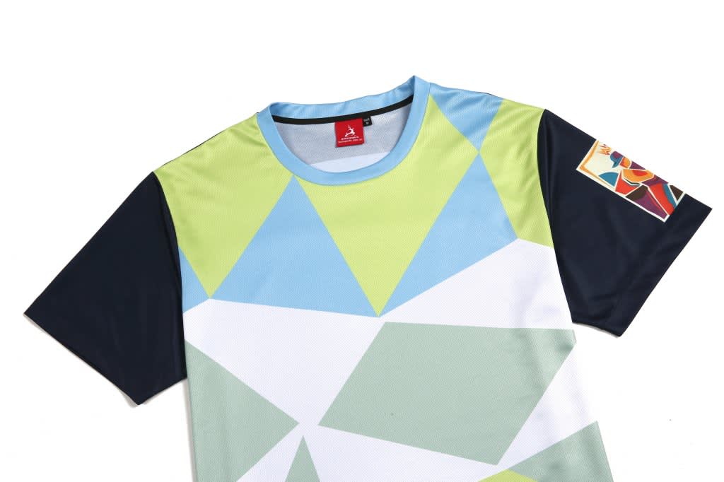 A colourful t-shirt featuring geometric patterns in light blue, green, and navy with a logo on the sleeve.