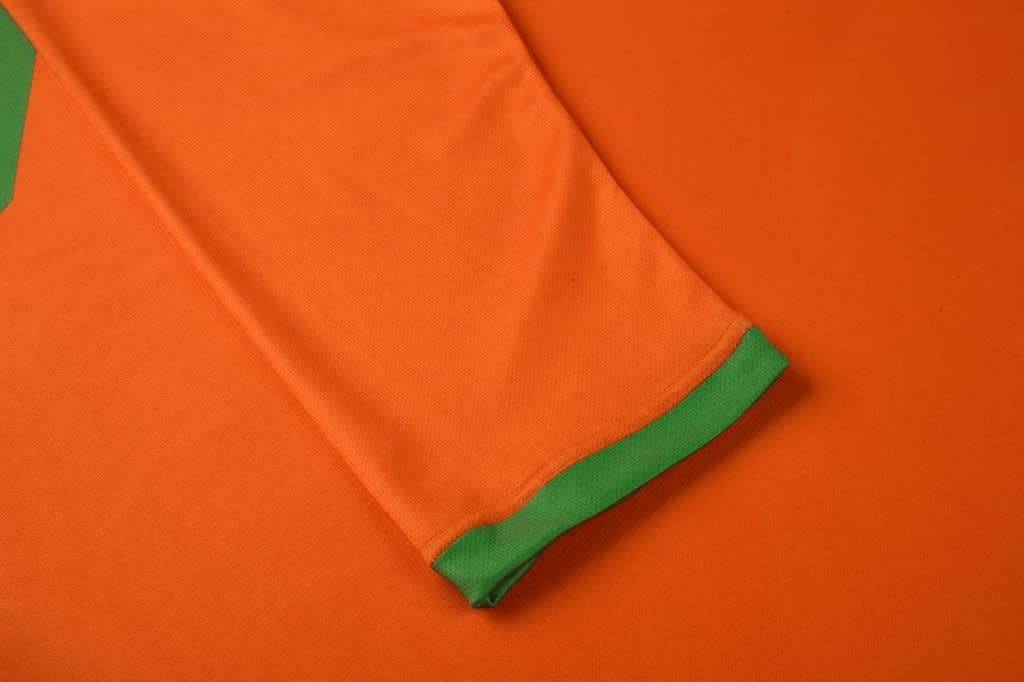 An orange garment with a green trim at the sleeve, laid flat on a matching orange background.
