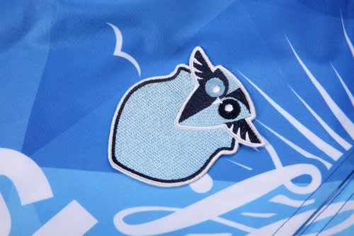 A blue beach shirt featuring a light blue patch with a stylised bird design and a logo.