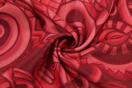 A red patterned fabric featuring intricate swirls and designs, suitable for creating sports uniforms like jerseys.