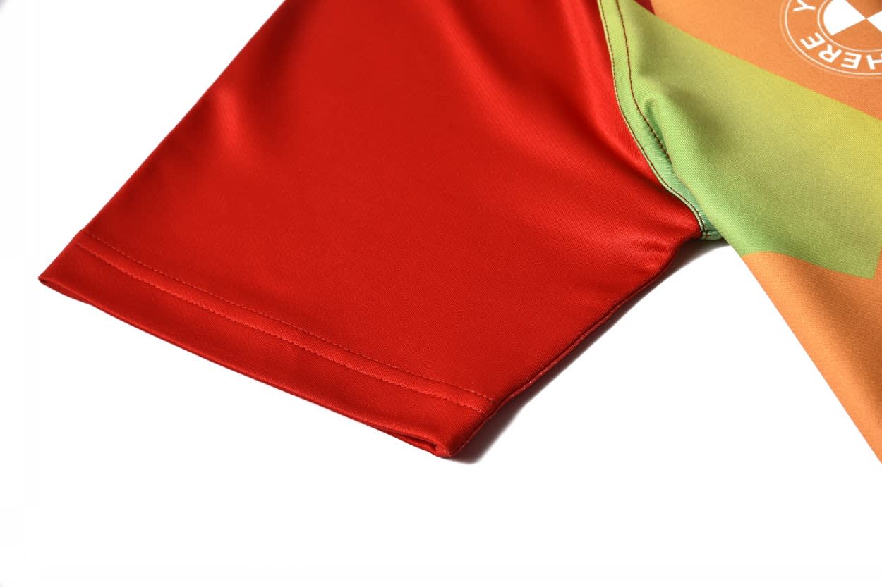 A vibrant football jersey featuring red sleeves and a multicoloured body design, with a logo present.