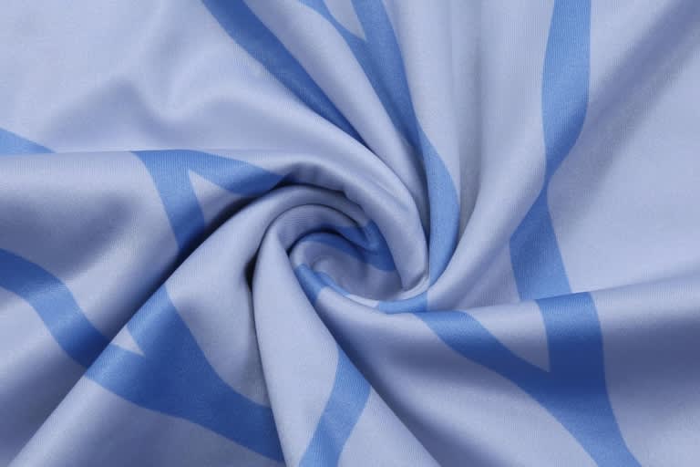 A folded fabric in light blue with a swirling pattern, featuring shades of darker blue. The material appears soft and smooth.