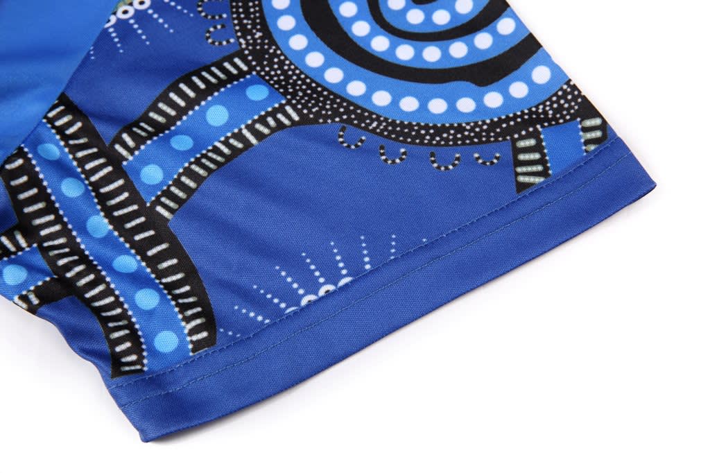 A blue sublimated T-shirt featuring Aboriginal artwork with intricate patterns and a black logo.