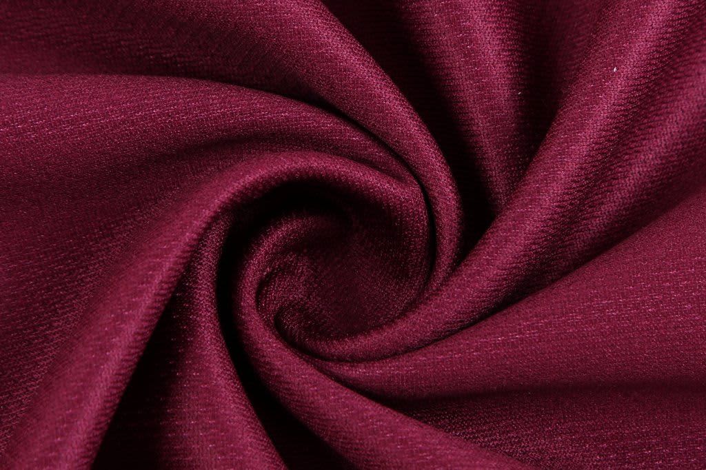 A close-up of deep burgundy fabric twisted in a spiral, showcasing its texture and rich colour.