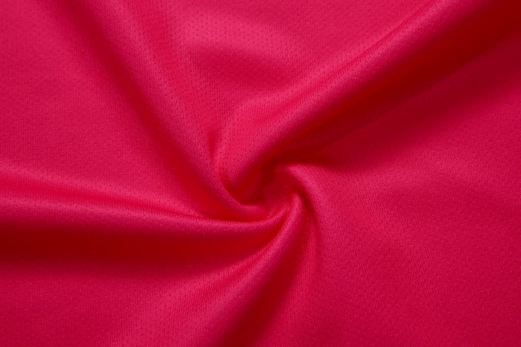 A close-up of smooth, pink fabric, showing its texture and weave pattern. It features a soft and vibrant appearance.