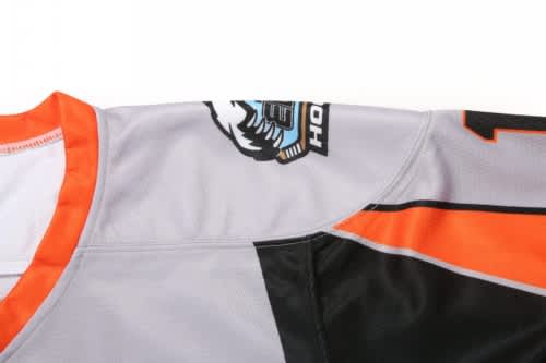 A grey and orange ice hockey jersey featuring a logo on the shoulder and a contrasting black design.