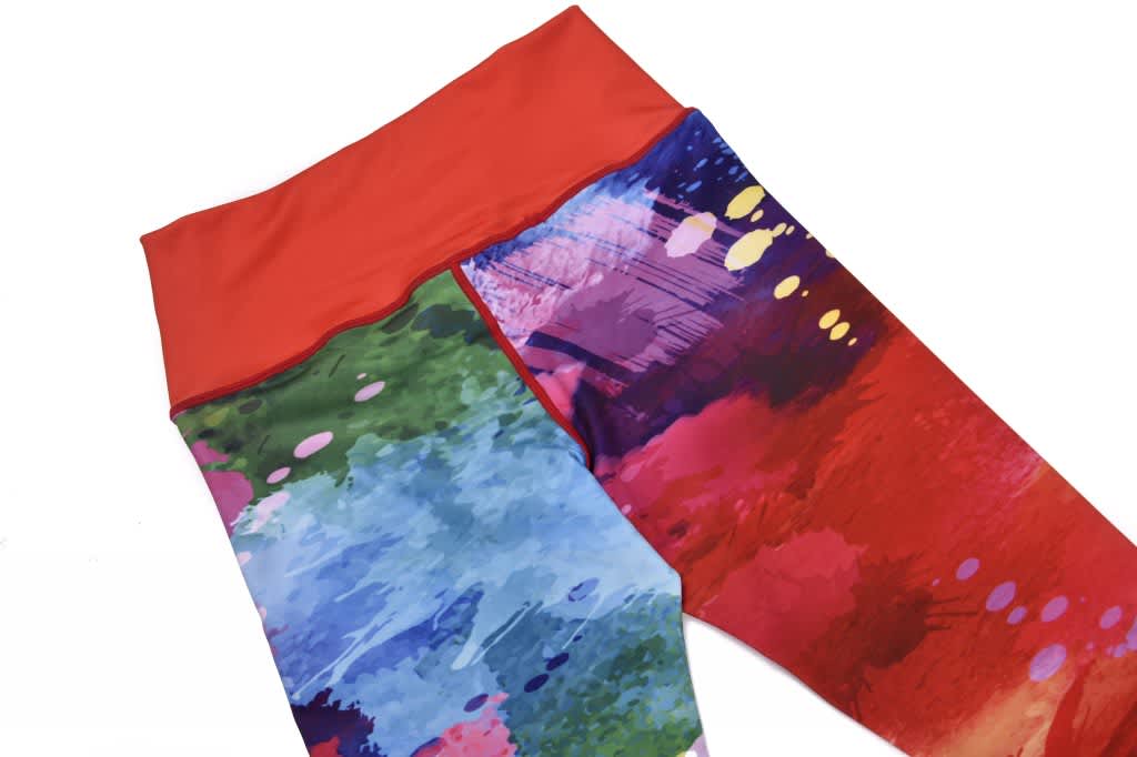 A pair of vibrant leggings featuring a blend of red, green, and blue abstract patterns with a solid red waistband.