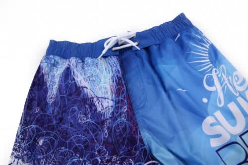 A pair of blue beach shorts featuring a mix of patterns and a drawstring waistband, with a logo visible.