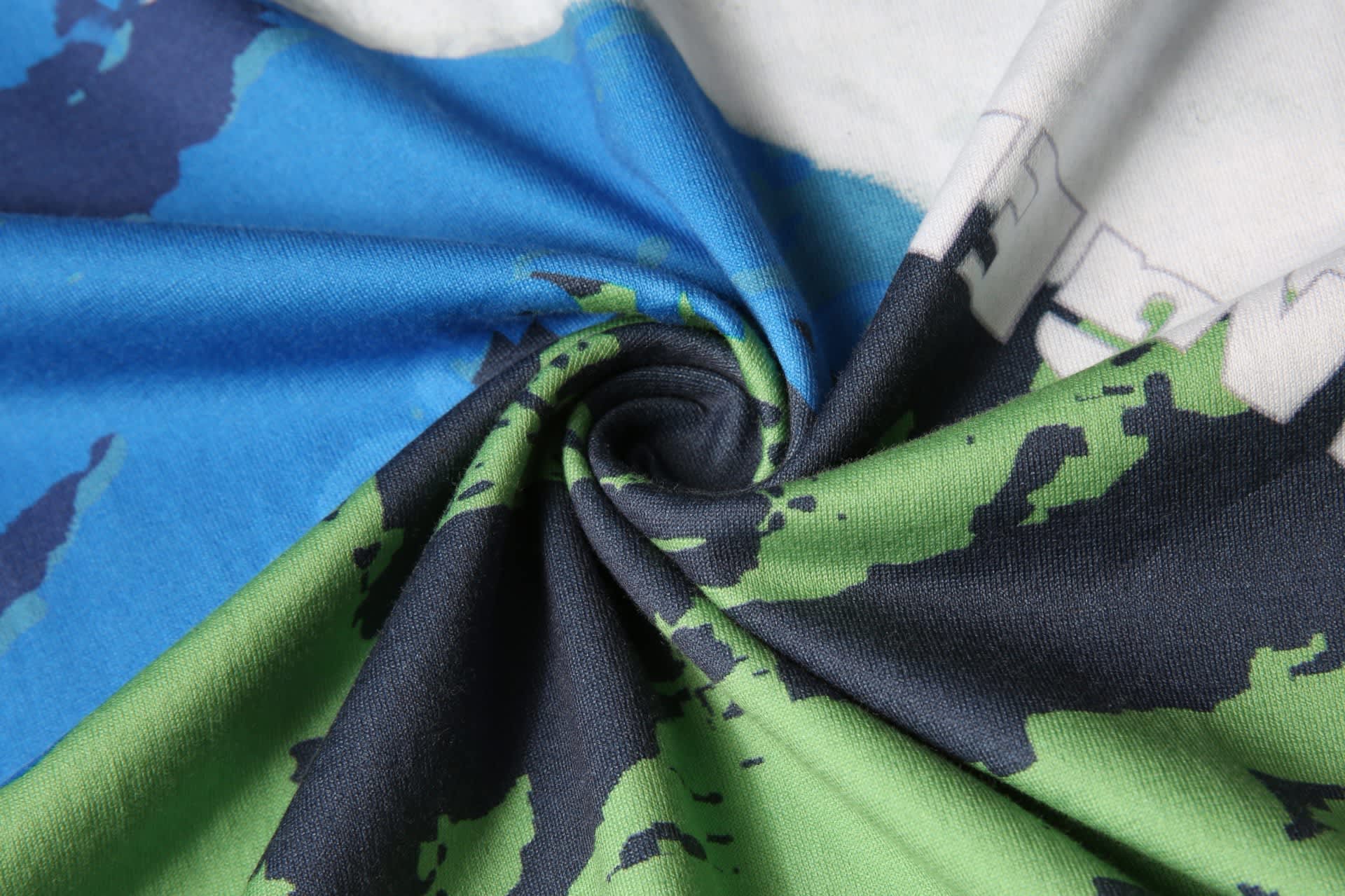 A close-up view of a custom cotton tee featuring blue and green fabric with a swirling pattern. The shirt has a logo.