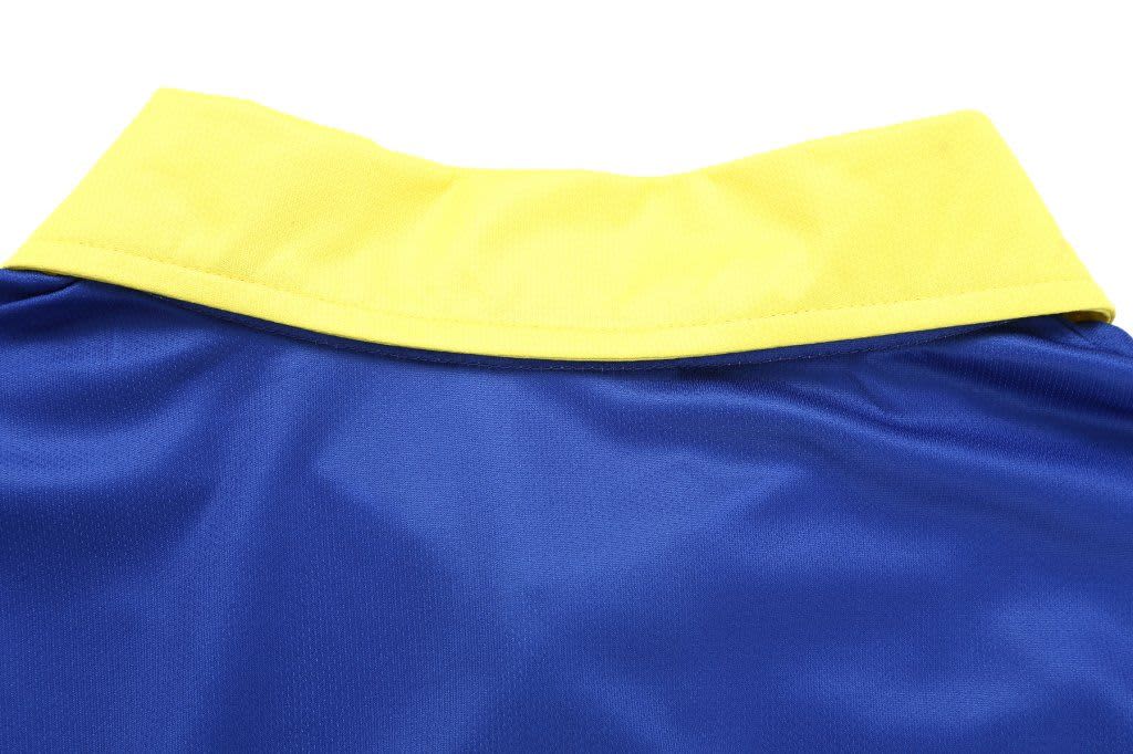 A blue cricket polo shirt with a yellow collar, featuring stitching details and a smooth fabric texture.