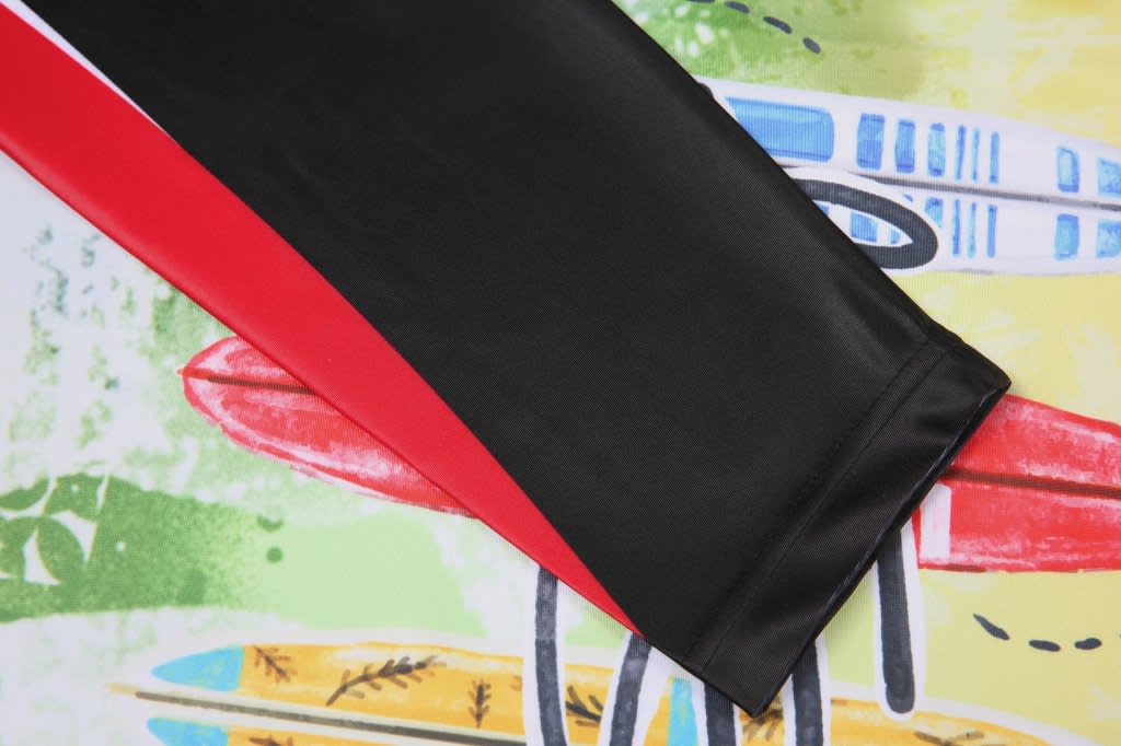 A black and red sublimation rashie club tee laying on a colourful surfboard-themed background.