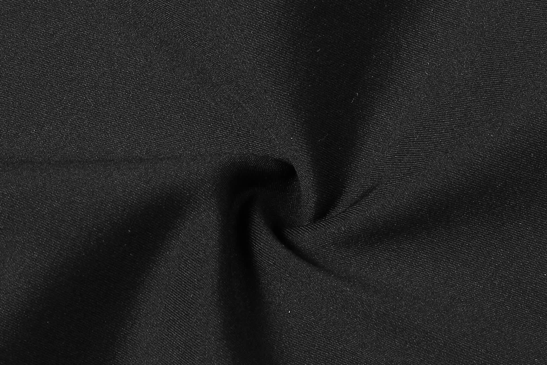 A close-up of black fabric, showcasing a smooth texture and a spiral fold pattern.
