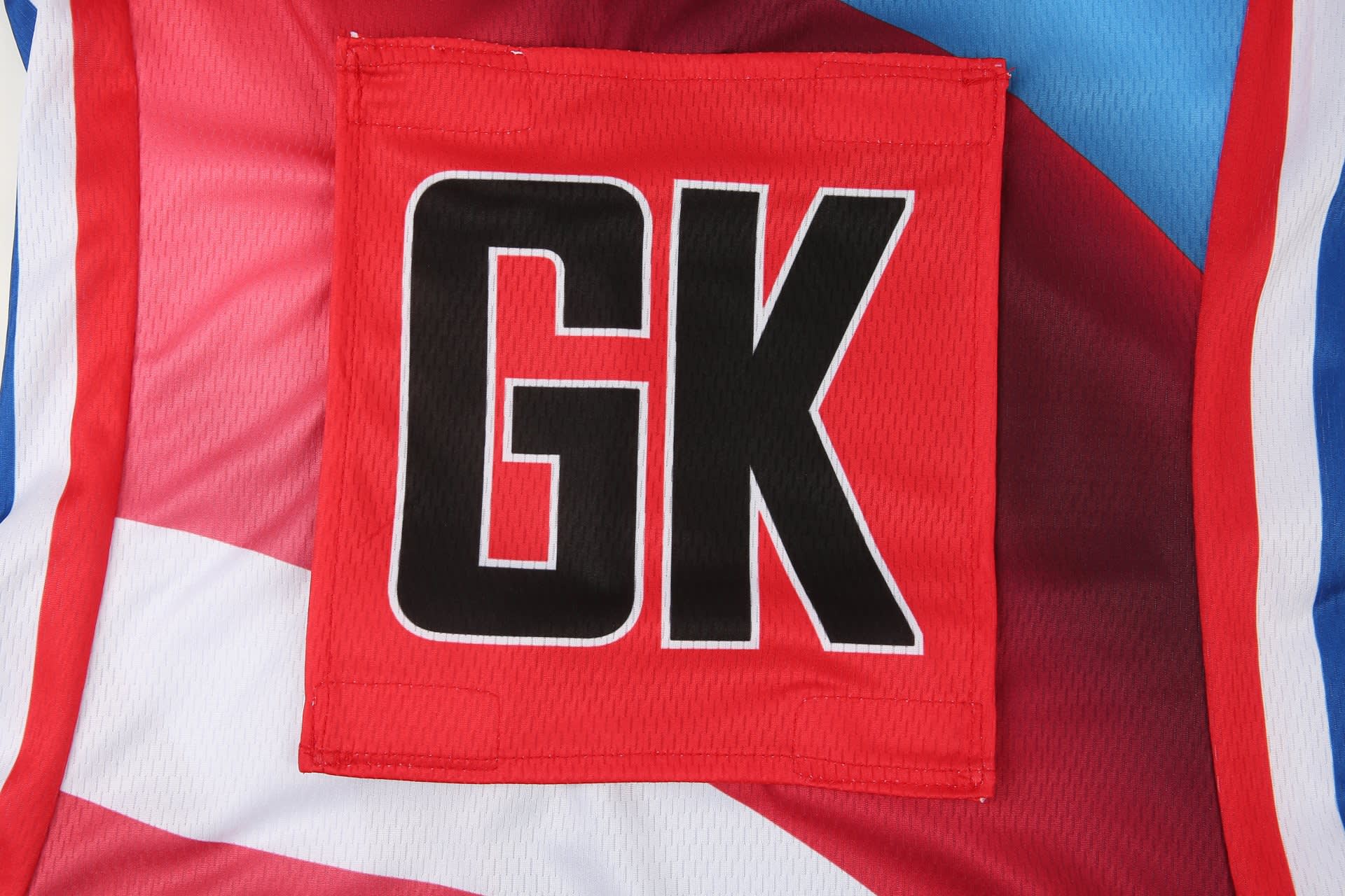 A red netball dress featuring a large black "GK" on a multicoloured background with blue and white accents.