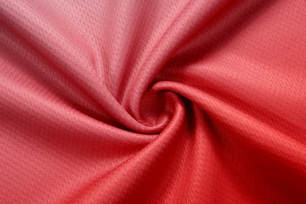 A close-up of soft, textured red fabric, featuring a smooth spiral drape.