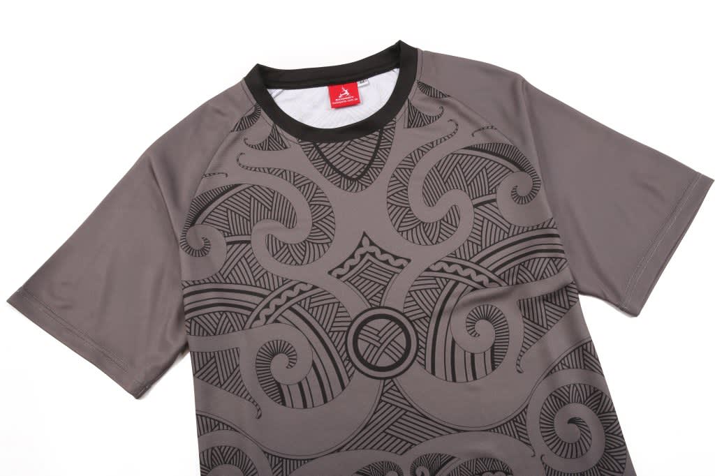 A grey jersey with intricate black patterns and a logo at the collar. It has short sleeves and a round neck.