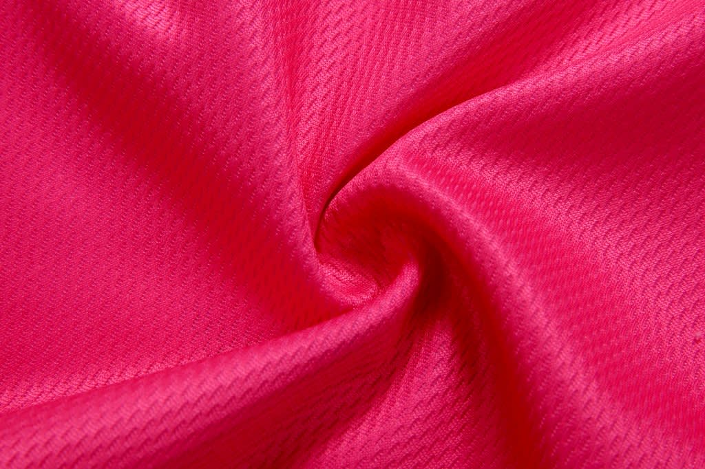 A close-up of pink textured fabric, showcasing a smooth and shiny finish, suitable for volleyball shorts.