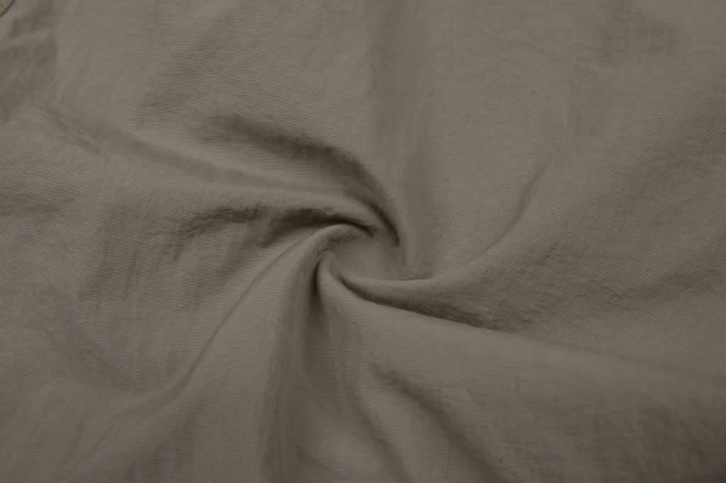 A fabric swatch of light beige windbreaker pants, featuring a smooth texture and a subtle spiral fold.