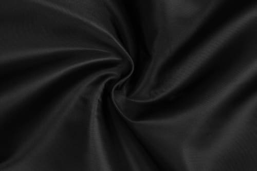 A close-up view of black fabric, displaying a smooth and flowing texture, with folds creating a swirl pattern.
