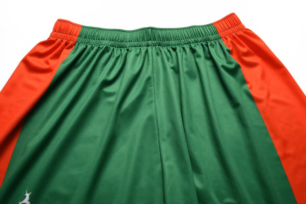 Green and orange junior soccer shorts with an elastic waistband and a logo on one side.