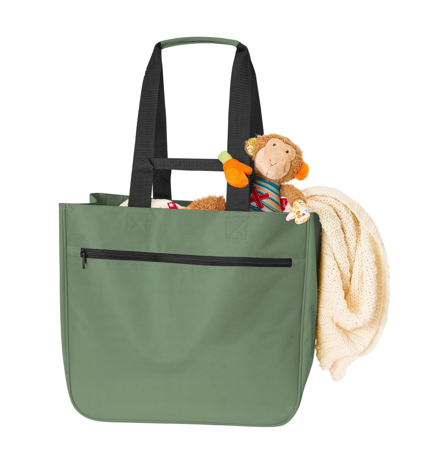 A green tote bag with black straps, featuring a stuffed monkey and a blanket inside.
