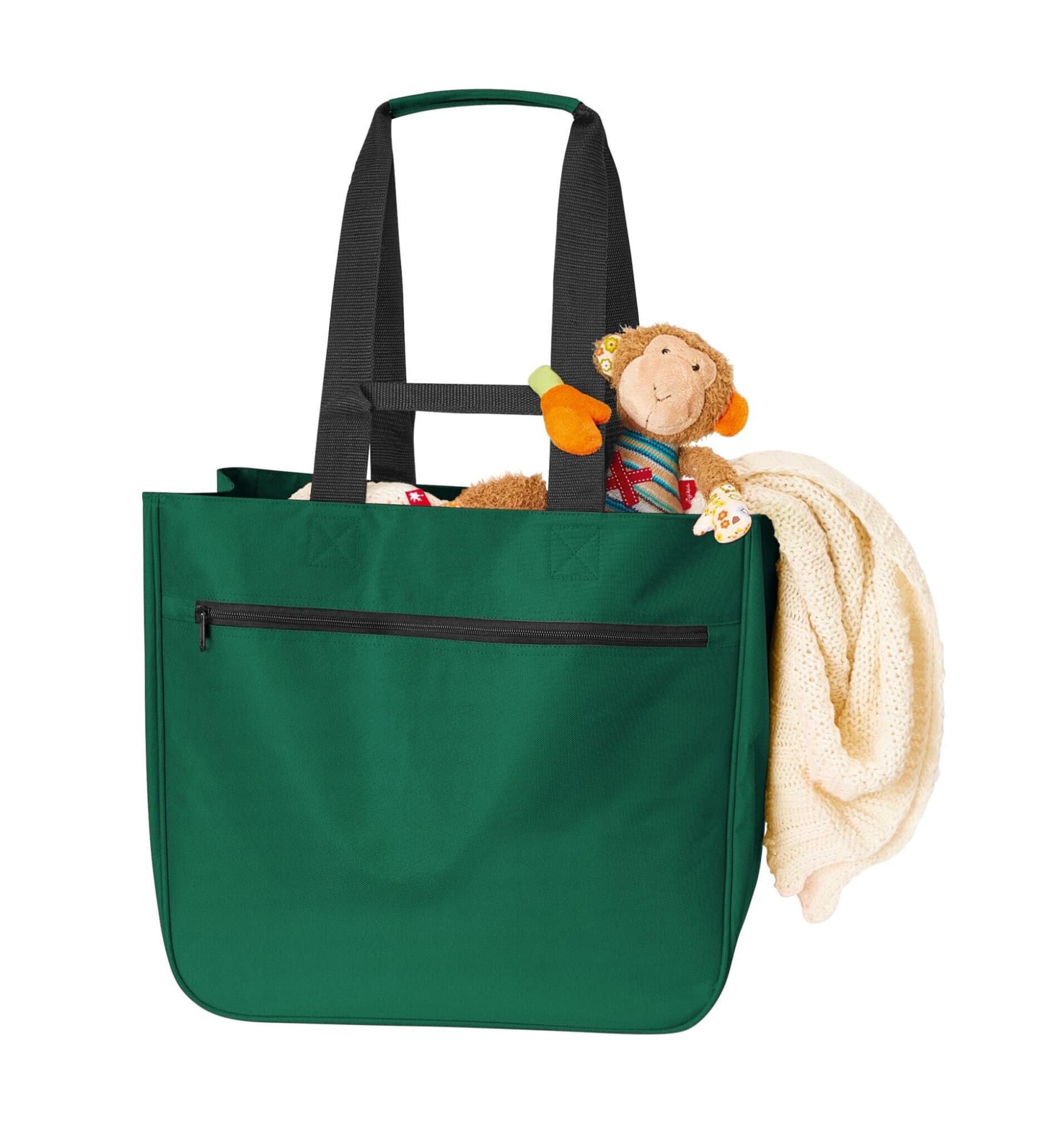 A green tote bag with black handles contains a plush monkey toy and a beige blanket. It has a front zip pocket.