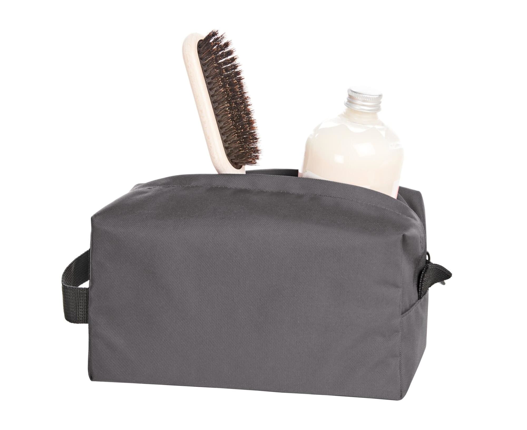 A grey toiletry bag containing a brush and a bottle, featuring a handle and a logo.