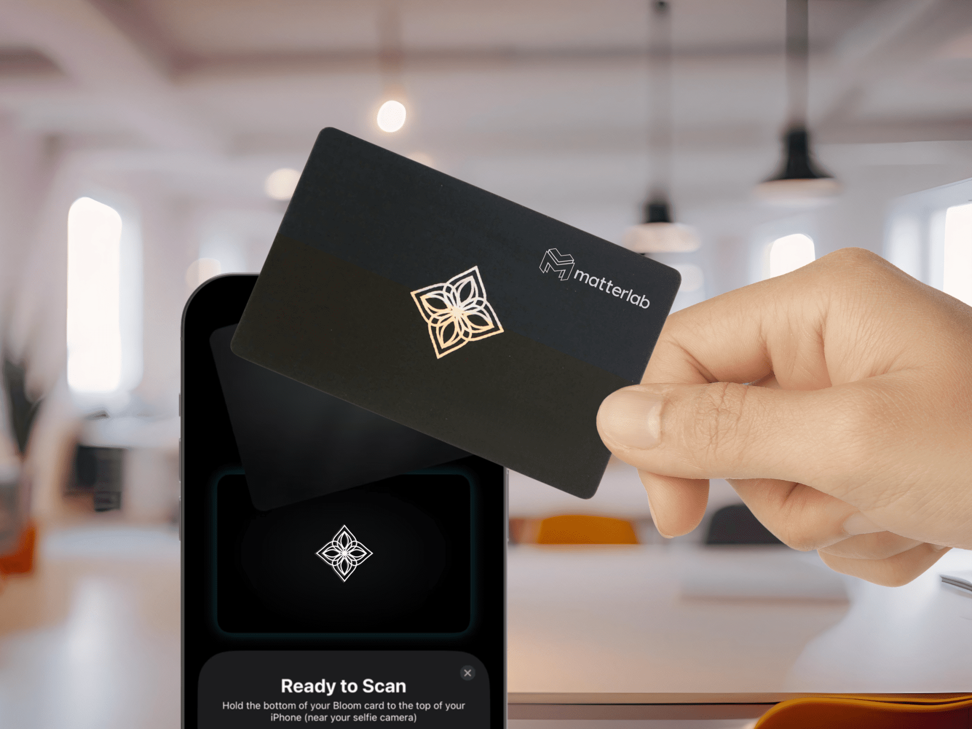 A hand holds a black card with a logo, positioned above a smartphone displaying a scanning interface.