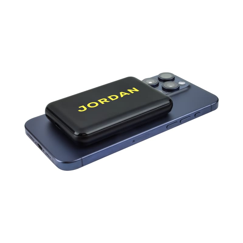 A black power bank with yellow branding, placed on a blue smartphone, showcasing its compact design.