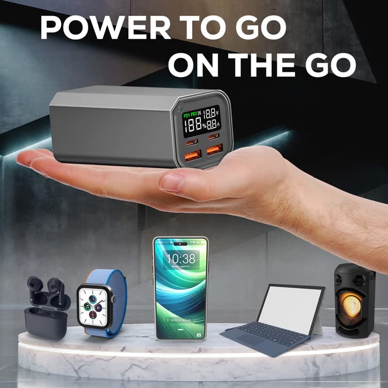 A sleek grey power bank held in a hand, featuring USB ports and an LED display, alongside various tech devices.